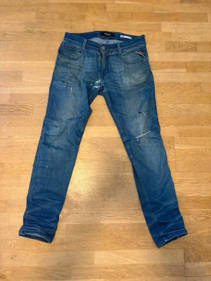 Blå slim fit jeans från Replay - Snygga blå slim fit jeans från Replay, modell Anbass. Jeansen har slitna detaljer och dragkedja i gylfen. Klassisk femficksdesign och lätt tvättad look för en trendig stil. Archive L32