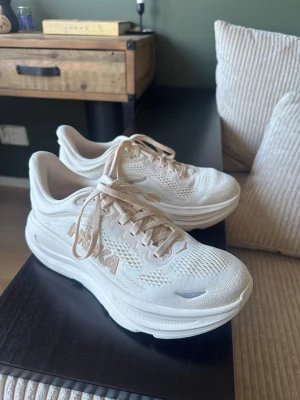 Beige Hoka sneakers med tjock sula - Säljer ett par beiga sneakers från Hoka med chunky sula och ventilerande mesh-ovandel. Skorna har klassisk snörning och diskret Hoka-logga på sidan. Perfekta för dig som gillar sportig stil och vill ha riktigt bekväma skor till vardags. Använde dessa skor endast 2 gånger inomhus, insåg ganska snabbt att dom är för stora för mig, hunnit kasta originalförpackningen och kan därav inte returnera vara till butik enl butikens regler. 