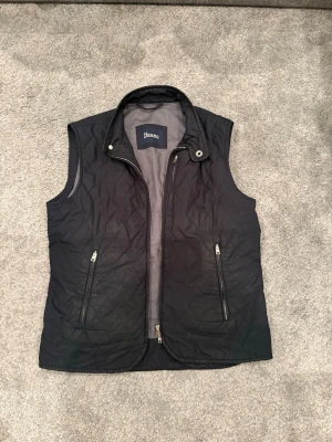 Herno dunväst - Snygg svart dunväst från Herno med quiltat mönster och två dragkedjeförsedda fickor framtill. Västen har hög krage och dragkedja hela vägen upp. Perfekt för lager på lager och en clean look.