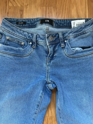 Blå bootcut jeans från LTB low waist - Snygga blå bootcut jeans från LTB, modell VALERIE. Klassisk femficksdesign med knappgylf och bälteshällor. Jeansen har en lätt tvättad look och är tillverkade i mjukt denimtyg som sitter skönt. Perfekta för dig som gillar en avslappnad men trendig stil.