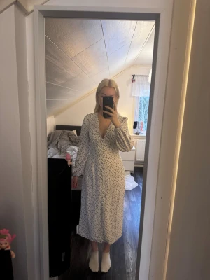 Lila & vit långklänning - Lilablommig vit klänning med knappar framtill och dragkedja på sidan, liknar adoore. Superfin till midsommar eller mösspåtagning!                      Köptes begagnat men har prislappar kvar🩷