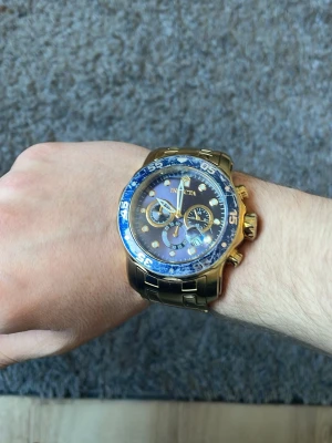 Guldfärgad klocka från Invicta - Snygg guldfärgad klocka från Invicta med blå urtavla och gulddetaljer. Klockan har flera små urtavlor, robust länkarmband i metall och tydliga siffror på bezeln. Perfekt accessoar för dig som vill sticka ut med en exklusiv look.