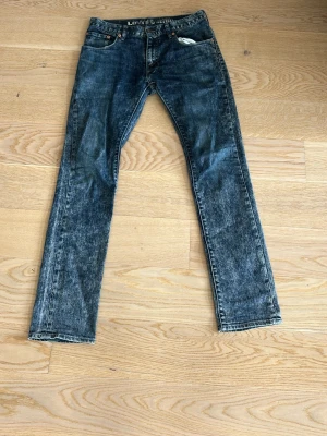 Levi's Denim raka blå jeans - Säljer ett par klassiska raka jeans från Levi's Denim i tvättad blå färg. Jeansen har fem fickor, knappgylf och tydliga slitningar för en cool vintagekänsla. Perfekta för dig som gillar tidlös streetstil och vill ha ett par jeans som funkar till allt.