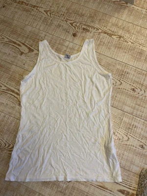 Vitt linne - Klassisk vit linnetopp i bomull med rund halsringning och ärmlös design. Perfekt basplagg som passar till allt och har en enkel, clean look. Skön och lätt att bära under varma dagar eller som lager under andra plagg. Storlek M