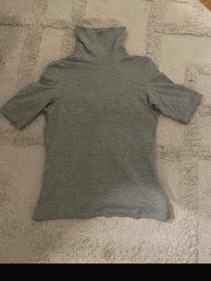 Grå polotopp från Monki - Grå polotopp från Monki i mjuk bomull. Toppen har korta ärmar och en hög polokrage