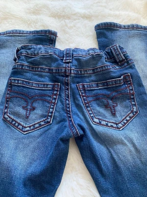 Blå jeans från Gina Tricot, stl 152 - Snygga blå jeans från Gina Tricot med röda kontrastsömmar och broderade bakfickor. Klassisk femficksmodell i stretchigt denimtyg. Perfekta för dig som gillar en avslappnad men trendig look.