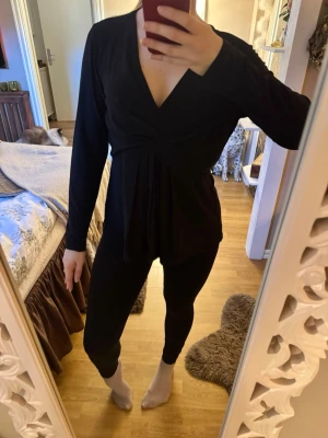 Svart v-ringad långärmad topp - Svart långärmad topp med djup v-ringning och snygga draperingar framtill. Modellen har en lösare passform nedtill och är tillverkad i ett mjukt, stretchigt material som känns skönt mot huden. Skulle gissa att det är storlek L, lappen är borta.