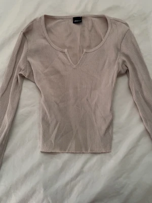 Ljusbeige långärmad topp - Trendig ljusbeige topp från Gina Tricot med lång ärm och snygg v-ringning med liten slits framtill. Perfekt att matcha med jeans eller kjol för en enkel men stilren look.