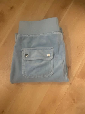 Ljusblå velourbyxor Juicy Couture - Säljer ett par ljusblå mjukisbyxor från Juicy Couture i mjuk velour. Perfekta för en chill och trendig look. (Sytt upp dom lite grann för dom var för långa på mig, jag är 164cm och dom passar parfekt på mig nu efter jag har sytt upp dom)