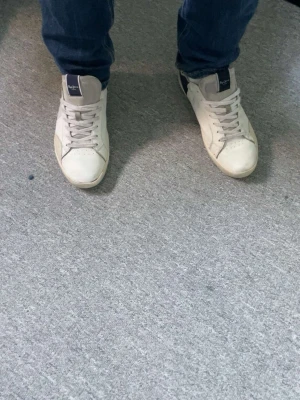 Vita och marinblå sneakers från pepe jeans - Snygga vita sneakers från pepe jeans med marinblå detaljer på häl och plös. Klassisk låg modell med vita snören och diskret logga på sidan. Tillverkade i slätt läder och textil för en clean look. Populära och riktigt feta skor som passar till allt!