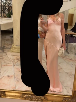 Satinklänning - Elegant ljusrosa klänning i satin med v-ringning och slits i sidan. Den är justerbar i ryggen med snören. Använd 1 gång.