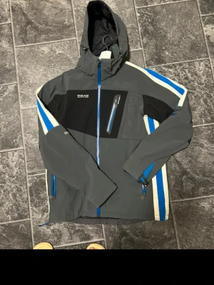 Grå vindjacka från 8848 Altitude - Snygg grå vindjacka med svarta och blå detaljer från 8848 Altitude. Jackan har huva, dragkedjor i blått, bröstficka och två sidofickor. Jackan är vattenavisande. Ny pris ca 3000~4000. In princip oanvänd. Jackan ligger ute på flera sidor så hör gärna av er innan🥰
