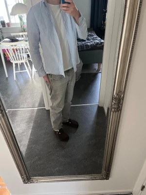 Ljusblå randig linneskjorta - Säljer en ljusblå skjorta från Dressmann i linne med tunna vita ränder. Skjortan har klassisk krage, diskreta knappar framtill och lång ärm. Perfekt för en avslappnad men ändå stilren look.