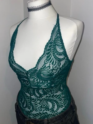 Grön spetsbody med djup urringning - Snygg grön body i genombruten spets med djup urringning och tunna axelband. Kroppsnära passform och vackert mönstrad spets ger en feminin look. Perfekt att styla med jeans eller kjol för en trendig outfit.