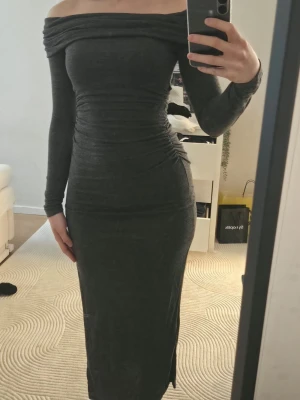 Mörkgrå offshoulder långklänning Bershka - Säljer en mörkgrå långklänning från Bershka med offshoulder-design och långa ärmar. Klänningen har en tight passform och är tillverkad i mjukt stretchigt material som framhäver figuren. Perfekt för dig som gillar stilrena och trendiga plagg.