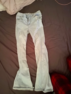 Ljusblå utsvängda jeans - Säljer ett par ljusblå jeans med utsvängda ben och klassisk femficksmodell. Jeansen har hög midja och är tillverkade i denim. Perfekta för dig som gillar retrostil och vill ha ett par riktigt snygga jeans med 70-talsvibbar. Finns blekningsfläckar 