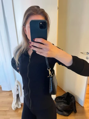 Svart axelväska  - Snygg svart axelväska med mönstrad yta och guldfärgade metalldetaljer. Väskan har en kompakt, rektangulär form och är väldigt stilren. 