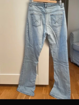 Ljusblå bootcut jeans  - Säljer ett par ljusblå jeans med bootcut passform och klassiska fem fickor. Jeansen har dekorativa sömmar på bakfickorna och är tillverkade i mjuk denim. Perfekta för en avslappnad och trendig look.