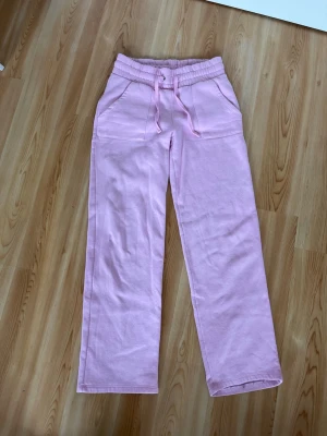 Ljusrosa mjukisbyxor med raka ben - Säljer ett par ljusrosa mjukisbyxor med raka ben och resår i midjan samt dragsko. Byxorna har stora fickor fram och bak, perfekta för en chill och avslappnad stil. Tillverkade i mjukt och bekvämt material som passar perfekt för hemmamys eller häng med vänner.