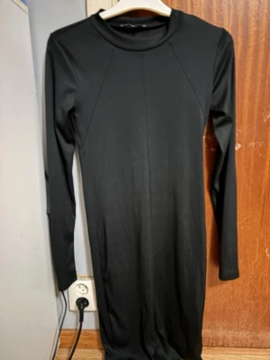 Svart långärmad klänning Gina Tricot storlek S - En stilren svart klänning från Gina Tricot med lång ärm och rund halsringning. Klänningen har en kroppsnära passform och är tillverkad i ett mjukt, stretchigt material som känns bekvämt mot huden. Perfekt för dig som gillar minimalistisk och clean stil. Storlek S