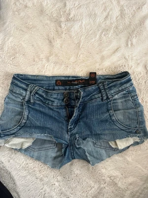 Blå jeansshorts från Karma - Säljer ett par blå jeansshorts från Karma med slitna detaljer och rå kant. Har sytt in dom i skrevet.