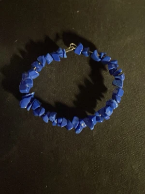 Blått armband med oregelbundna pärlor - Snyggt armband med starkt blå oregelbundna pärlor i plast eller sten. Pärlorna sitter tätt på en tråd och ger ett coolt, unikt intryck. Perfekt accessoar för dig som vill sticka ut med färg och form.OBS! Materialet är okänt, kan ej garantera att det är rostfritt.
