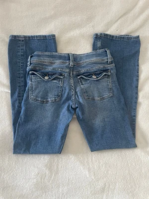 Blå jeans med fickdetaljer - blå jeans med raka ben/lite utsvängda och snygga fickdetaljer bak. Slitna ner till. Mellan hög midja. Gina trico Young i storlek 152.