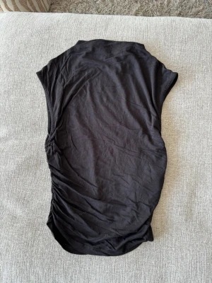 Svart ärmlös topp i bomull - En enkel svart ärmlös topp i mjuk bomull. Modellen har en rak passform, perfekt att matcha med jeans eller kjol. Stilren och lätt att bära till olika outfits.