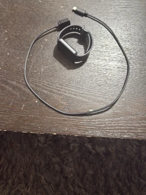 Svart Huawei smartklocka med laddare - Säljer en svart Huawei smartklocka med rektangulär skärm och silikonarmband. Klockan har färgdisplay som visar tid, steg, puls och batterinivå. Laddkabel medföljer. Perfekt för dig som vill ha koll på träning och hälsa.