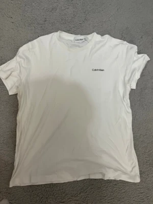 Vit t-shirt från Calvin Klein - Säljer en klassisk vit t-shirt från Calvin Klein med diskret logga på bröstet. T-shirten har rund halsringning och korta ärmar. Tillverkad i mjuk bomull för en bekväm känsla och enkel stil.