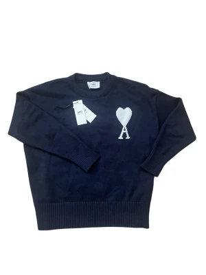  Ami tröja  - Mörkblå stickad tröja från Ami med rund halsringning och ribbade muddar. På bröstet finns ett vitt hjärta med bokstaven A under, vilket är Ami:s ikoniska logga. Tröjan har en klassisk passform och är tillverkad i mjukt material. Tags med följer kan gå ner i pris vid snabb affär. 