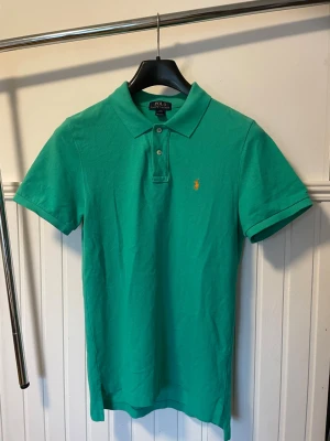 Ralph Lauren grön polo piké  - Ralph Lauren polo piké i en väldigt härlig grön färg med orange häst, tröjan är knappt använd, pris kan diskuteras vid snabb affär.