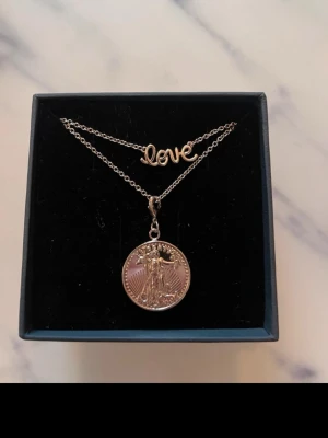 Halsband från Mockberg  - Snyggt halsband i silverfärg med två hängen, myntet är avtagbart.  Kedjan är tunn och elegant, perfekt för att ge din outfit en personlig touch. Passar dig som gillar stilrena och trendiga accessoarer. Helt nytt