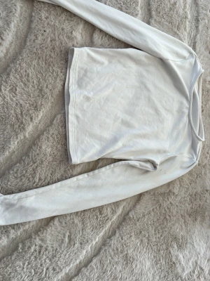 Vit långärmad basic tröja - En enkel vit långärmad tröja med rund halsringning. Tröjan har en rak passform och är tillverkad i ett mjukt, stretchigt material som passar perfekt till lager på lager. Perfekt basplagg för alla tillfällen.