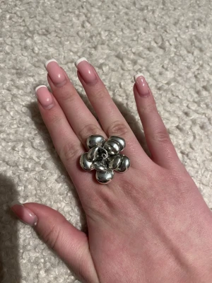 Stor silverfärgad blomring - Säljer en unik och iögonfallande ring i silverfärg med en stor blomformad design. Ringen har rundade, glänsande blad som ger ett coolt och trendigt uttryck. Perfekt för dig som vill sticka ut med dina accessoarer. Ringen är även justerbar!
