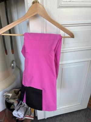 Rosa peak performance täckbyxor med svarta detaljer - Snygga rosa täckbyxor med svarta förstärkningar vid bensluten. Perfekta för vinterns alla äventyr och håller dig både varm och torr