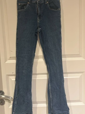 Blå bootcut jeans med slits - Säljer ett par blå bootcut jeans med slits vid bensluten. Jeansen har klassisk femficksmodell, mid rise midja och i storlek 164.
