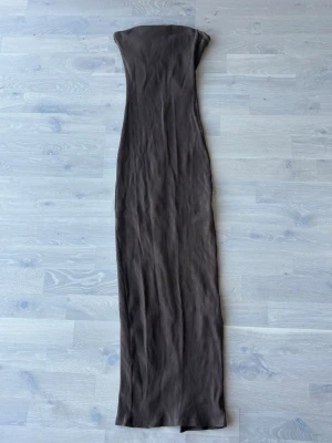 Brun ribbad axelbandslös maxiklänning - Säljer en brun, ribbad maxiklänning i stretchigt material. Klänningen är axelbandslös och har en lång, smal passform som ger en snygg siluett. Perfekt för dig som gillar minimalistisk stil och vill ha något enkelt men ändå trendigt.