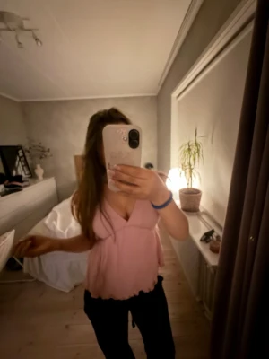 Ljusrosa v-ringad blus med volang - Söt ljusrosa blus med v-ringning och volangdetaljer vid ärmslut och nederkant. Blusen har korta ärmar och en flowy passform som ger en romantisk vibe. Perfekt att styla med jeans eller kjol för en trendig look. Använt fåtal gånger så är som ny! 