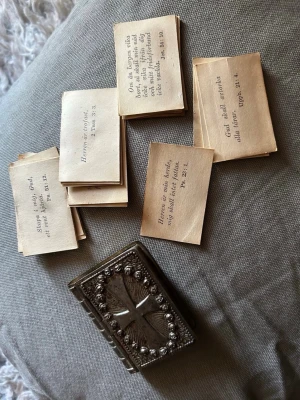 Antik ask med bibelcitatkort - Unik liten ask i metall formad som en bok med kors och dekorerade detaljer på locket. Innehåller flera små kort med bibelcitat på svenska. Perfekt för dig som gillar kristna samlarprylar eller vill ha en speciell inredningsdetalj.