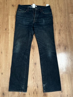 Mörkblå raka jeans från J.lindeberg - Snygga mörkblå jeans från J.lindeberg med rak passform och klassiska fem fickor. Jeansen har diskreta slitningar och kontrastsömmar, samt en läderpatch bak i midjan. Perfekta för en avslappnad och stilren look.