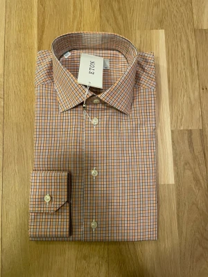 Rutig skjorta från Eton i strl 40 - Snygg rutig skjorta från Eton i contemporary fit. Skjortan är helt ny och är i original förpackning. Obs skjortan har ingen ficka utan det är ärmen som får det att de ut så. Nypris ca 1700 kr mitt pris endast 499 kr. Fraktar inom 1 dag, om du har någon fundering så är det bara att höra av sig😊