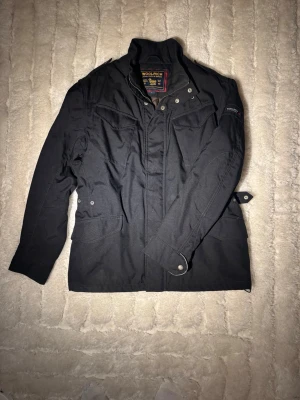 Svart woolrich jacka - Stilren och funktionell Woolrich jacka i svart. Klassisk design med flera fickor och högkvalitativa material – perfekt som vardagsjacka under höst/vår eller mild vinter.✔️ Märke: Woolrich ✔️ Storlek: L ✔️ Färg:Svart ✔️Passform: Normal ✔️ Skick: Mycket bra begagnat skick ✔️ Funktioner: Flera fickor, dragkedja + knäppning, justerbara ärmslut