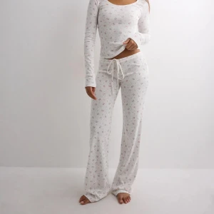 Cute print pants Nelly - Mysigt loungewear-set i vitt med små rosa blommor. Setet består av en långärmad topp med rundad hals och matchande byxor med dragsko i midjan. Materialet är mjukt och stretchigt, perfekt för avslappnade dagar hemma. Fick i julklapp men har inte använt speciellt mycket. Slutsålda från storlek xxs-medium därav priset ❤️nypris 300kr