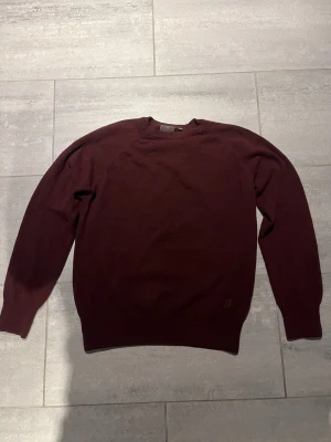 Vinröd stickad tröja med brodyr - Mysig vinröd stickad tröja med rund hals och långa ärmar. Tröjan har ribbstickade muddar och en diskret brodyr med bokstäverna 'OJ' nedtill. Perfekt för lager-på-lager och enkel att matcha med jeans.