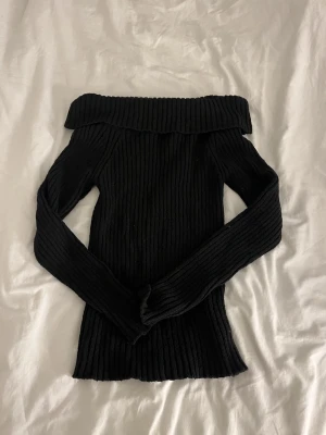 Svart off shoulder stickad tröja - Trendig svart stickad tröja med off shoulder-design och ribbstickat mönster. Relativt stretchig och knappt använd 