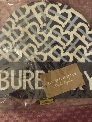 Burberry monogrammönstrad mössa - Säljer en snygg mössa från Burberry med ikoniskt monogrammönster i vitt och ljusblått på mörk botten. Mössan har en bred kant med BURBERRY-loggan framtill. Perfekt accessoar för dig som gillar exklusiv streetstyle och vill sticka ut. Oanvänd mössa 