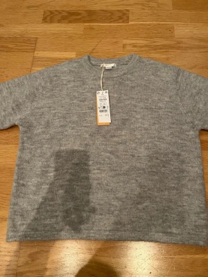 Ljusgrå stickad tröja Ginatricot - Mysig ljusgrå stickad tröja från Ginatricot med rund halsringning och ribbade muddar. Tröjan har en enkel och stilren design som passar perfekt till lager på lager och är tillverkad i mjukt material för extra komfort.