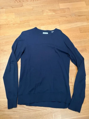 Mörkblå stickad tröja  - En stilren mörkblå stickad tröja från Jack & Jones med rund halsringning och långa ärmar. Tröjan har ribbade muddar vid ärmslut och nederkant, perfekt för en clean och enkel look. Storlek S. Använd endast fåtal gånger mycket fint skick. Tveka inte på att höra av dig vid frågor eller funderingar kring passform eller liknande! 