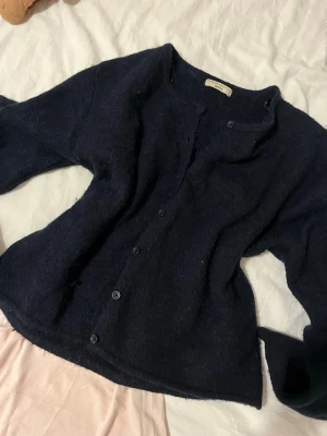 Svart kofta från Gina Tricot - Mysig mörkblå kofta från Gina Tricot i fluffigt stickat material. Koftan har rund halsringning, knäppning framtill med svarta knappar och långa ärmar. Perfekt för lager-på-lager och enkel att matcha med olika outfits.